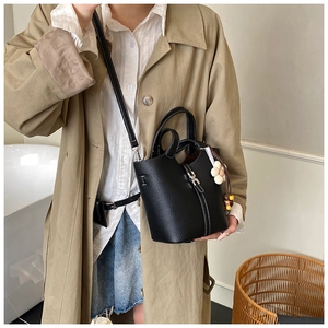 Detail of a black leather bucket bag with white stitching and floral charm on a trench coat