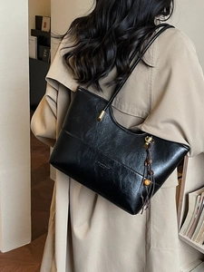 Classic black leather tote bag with gold hardware and tassel detail shown on model