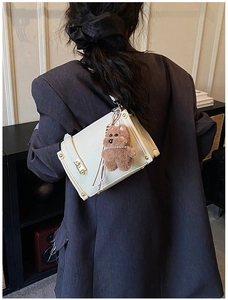 Detailed view of white lychee texture leather bag with gold clasp and brown bear charm