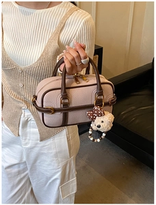 Détail du sac Boston en cuir beige texturé avec breloque ours et poignée marron