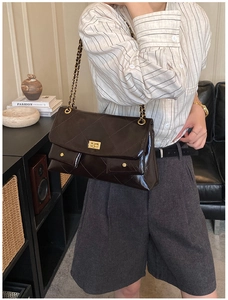 Detail of dark brown quilted leather bag with gold clasp and chain strap on a model