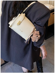 Detailed shot of beige lychee leather bag with gold lock and brown teddy bear charm