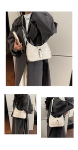 Detail view of cream leather shoulder bag with silver buckle on grey trench coat