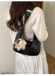 Detail of black faux leather dumpling bag with wide strap and beige plush pendant