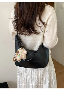 Detail of minimalist black crescent bag with vintage texture and a plush lamb pendant