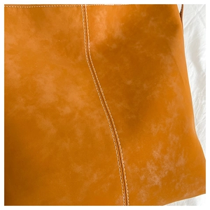 Detailed close-up of caramel leather tote bag with precise white contrast stitching