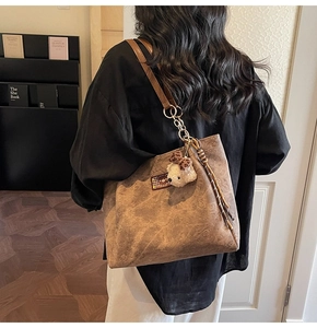 Close-up of a brown suede tote bag featuring embossed bear patterns and plush charm
