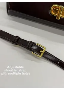 Detail of adjustable dark brown leather shoulder strap with golden buckle and holes