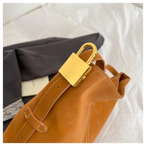 Detailed macro view of the golden square twist lock and white stitching on a brown leather bag