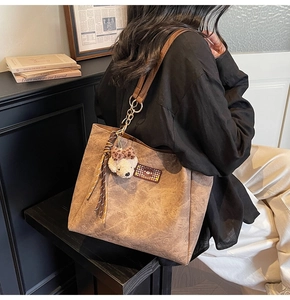 Detailed view of brown tote bag with embossed bear patterns and plush bear charm