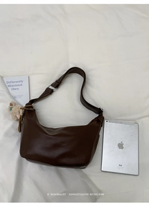 Minimalist brown crescent bag with plush bear charm showing medium capacity next to a tablet