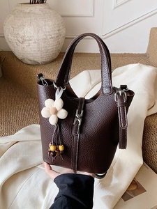Dark brown leather bucket bag with pebble texture and flower pendant on warm background