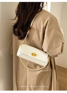 Detail of white leather underarm bag featuring a gold buckle and woven chain strap