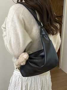 Minimalist black pleated hobo bag with plush lamb charm shown on a female model