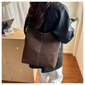 Detail of large brown tote bag with white stitching and gold lock on a desk
