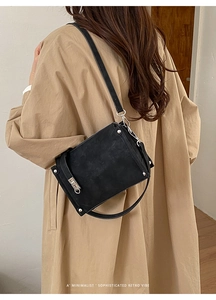 Detailed back view of a black retro baguette bag with silver rivets on a beige coat