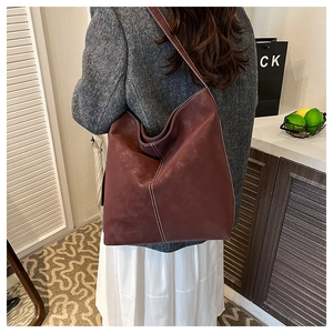 Detailed view of burgundy tote bag with white contrast stitching on model's shoulder