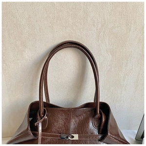 Detail of coffee brown glossy tote bag with silver metal buckle and oil wax texture
