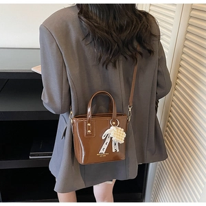 Detail einer braunen Eimer-Tasche mit Perlen-Spitzen-Charm an einem grauen Blazer