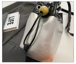 Detail of silver metallic bucket bag featuring black drawstring closure and wood bead