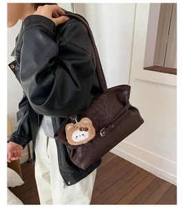 Close-up of deep coffee leather tote bag with metal buckles and plush animal charm