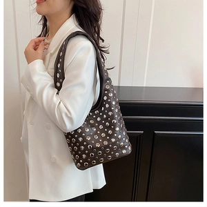 Détail d'un sac hobo en cuir noir avec rivets argentés porté sur un blazer blanc