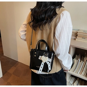 Rear view of glossy black mini bag featuring pearl heart and lace bow charms on shoulder