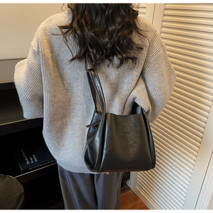 Detail of a chic black leather bucket bag with top handle worn over a grey knit sweater