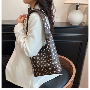 Détail du sac bandoulière en cuir marron foncé avec rivets argentés sur modèle en blazer