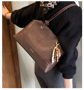 Detail of dark brown leather shoulder bag with glossy texture and beaded charm
