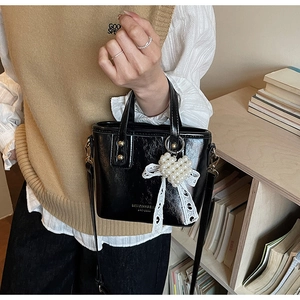 Detail der schwarzen Beuteltasche mit Perlenherz-Anhänger und Spitzenschleife aus PU-Leder
