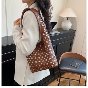 Détail d'un sac bandoulière en cuir marron à rivets argentés porté sur un blazer blanc