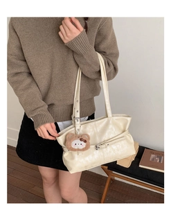 Detail view of cream white tote bag with adjustable straps and plush bear charm accessory
