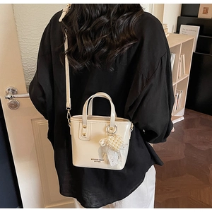 Fashionable beige bucket bag with pearl pendant shown in a stylish crossbody carry style