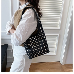 Gros plan sur un sac sous le bras en cuir noir avec clous argentés porté par un mannequin
