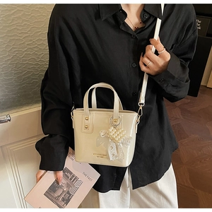 Detail der cremeweißen Mini-Beuteltasche mit Glanzeffekt und Perlenherz-Anhänger