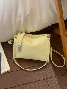 Minimalist pale yellow baguette shoulder bag with silver hardware on wood floor