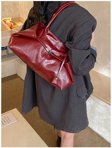 Detail of dark red tote bag with metal twist lock and glossy leather texture on model