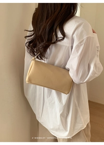 Close-up of minimalist beige pillow bag with silver metal ring and litchi grain texture