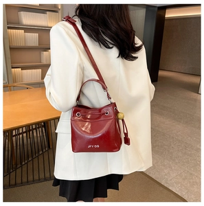 Red leather bucket bag featuring a drawstring closure and stylish wooden bead charm
