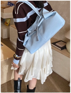 Model wearing a light blue soft leather tote bag with long straps in a cozy indoor setting