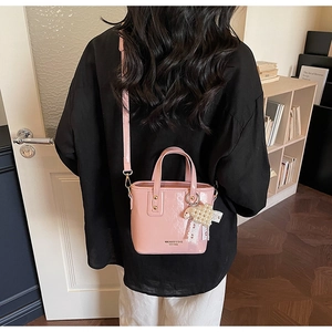 Detail of light pink patent leather bucket bag with pearl bow charm and logo text