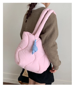 Detail of pink quilted puffer tote bag with blue plaid charm on shoulder of a model
