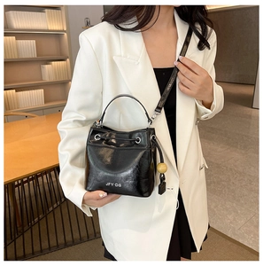 Detail of a black patent leather bucket bag with white logo and wooden ball charm