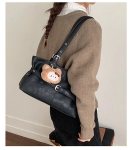Detail view of black faux leather tote bag featuring silver buckles and a cute bear charm