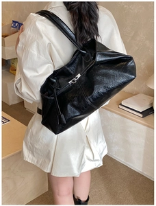 Detail of a black oil-wax leather tote bag with a silver buckle worn by a model