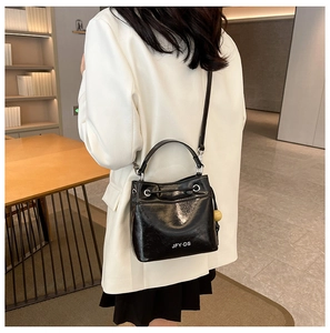 Detail of a shiny black bucket bag with white lettering and adjustable shoulder strap