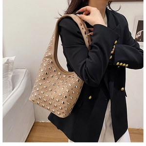 Detail of beige hobo bag with silver metal studs worn on shoulder over black blazer