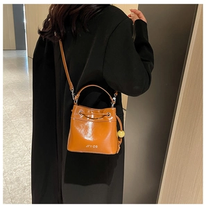 Detail of orange-brown bucket bag with drawstring closure and beaded charm on model