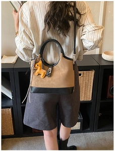 Detail of khaki suede tote bag with horse charm, ribbon decor and black leather handles